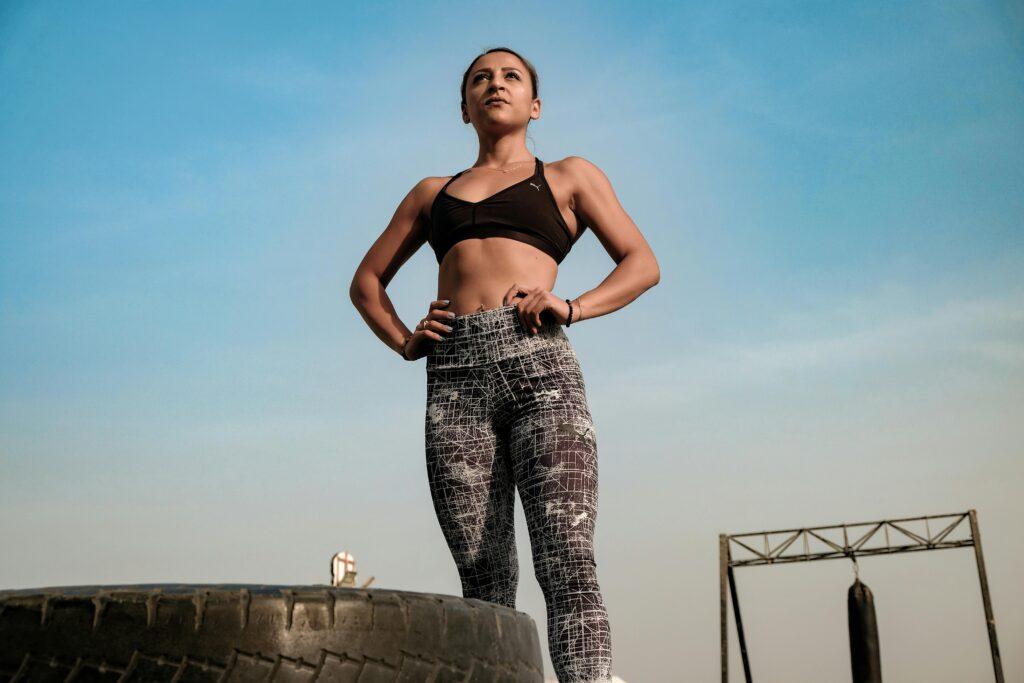 Empowered woman stands confidently on a tire outdoors, showcasing fitness and strength.
