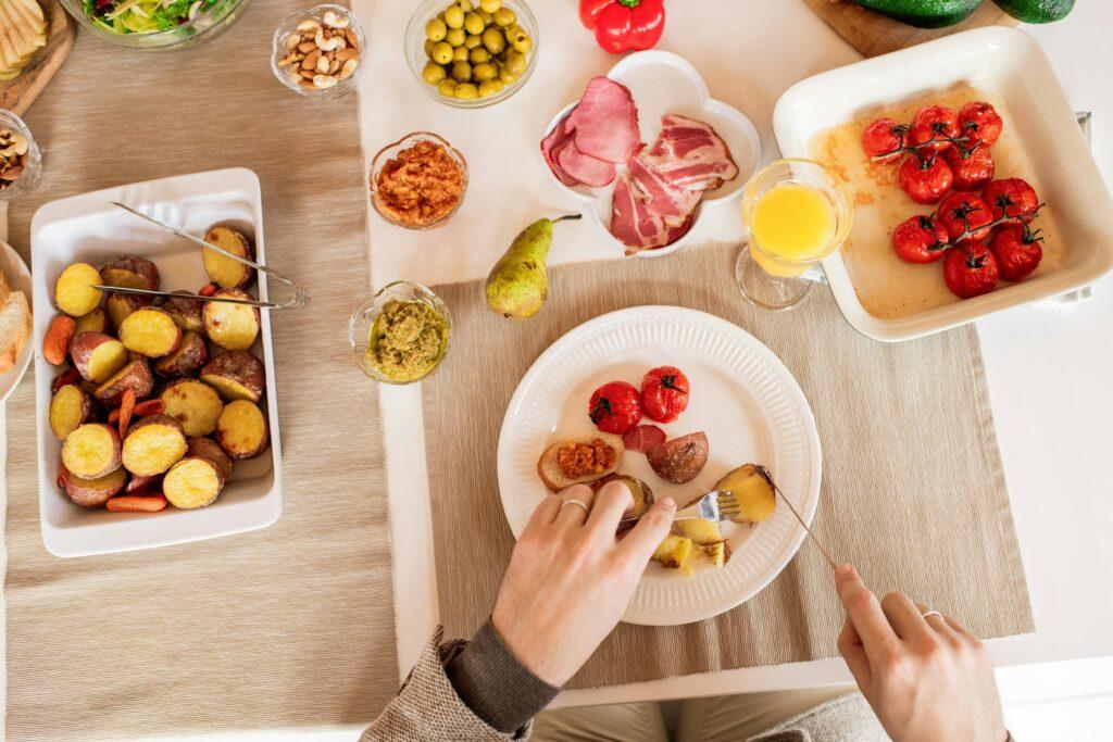 Top-down view of a vibrant brunch spread featuring roasted potatoes, tomatoes, cold cuts, and fresh juice.