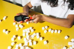 Close-up of a person testing blood sugar levels with a glucometer surrounded by sugar cubes.