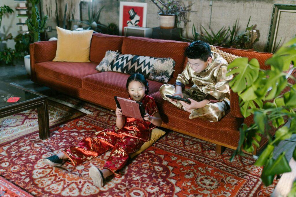 Two kids enjoying tablets on a colorful rug in a cozy living room setting.